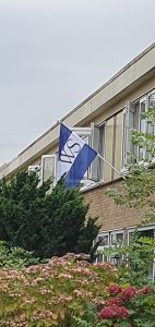 De naar links wapperende Weesper Vlag met WS dichterbij de mast